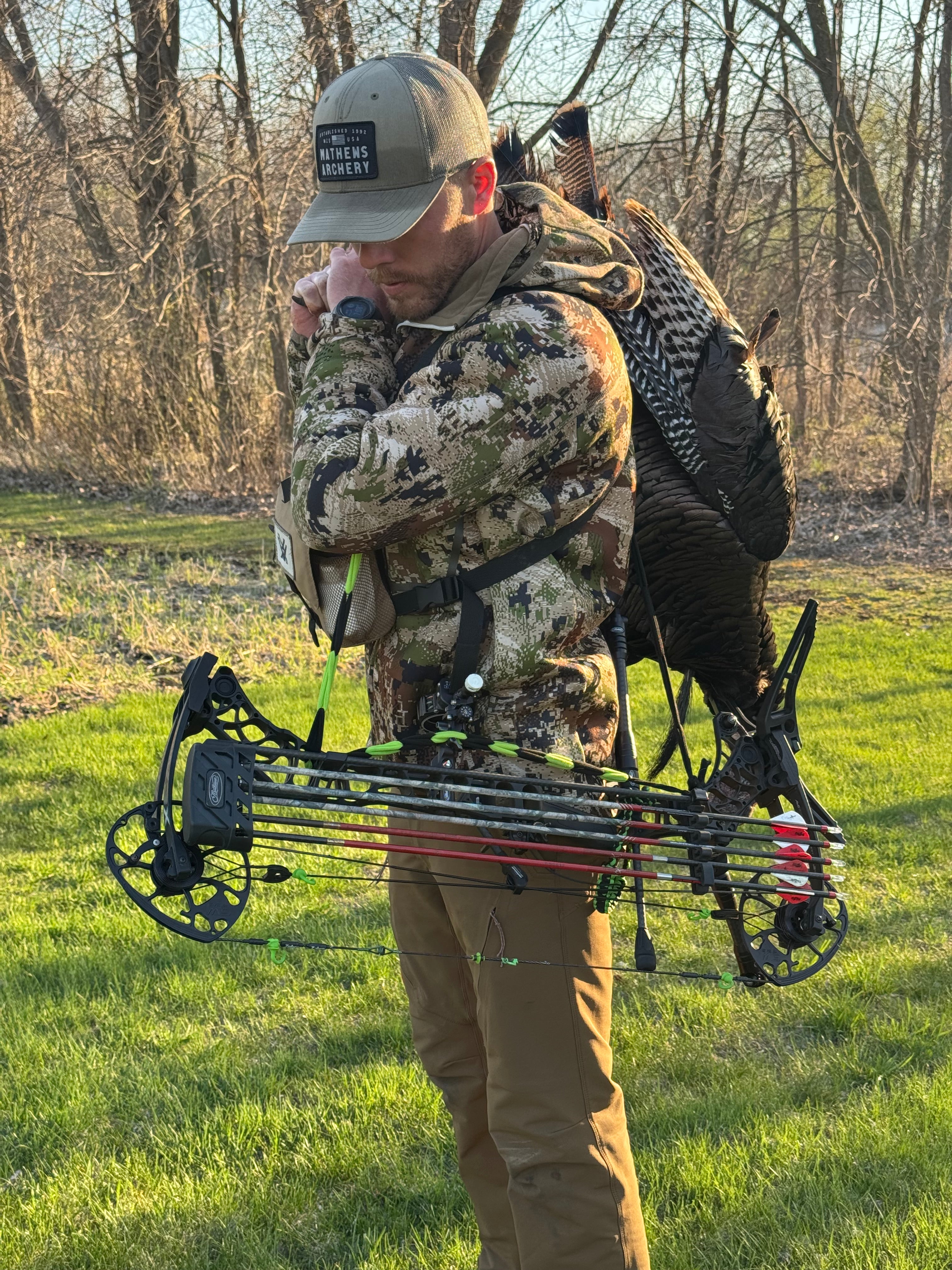 Hunter with a bow, vsling and a dead turkey in a grassy field