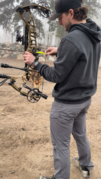 Person adjusting a bow outdoors on a dirt ground with Vsling on bow for shot