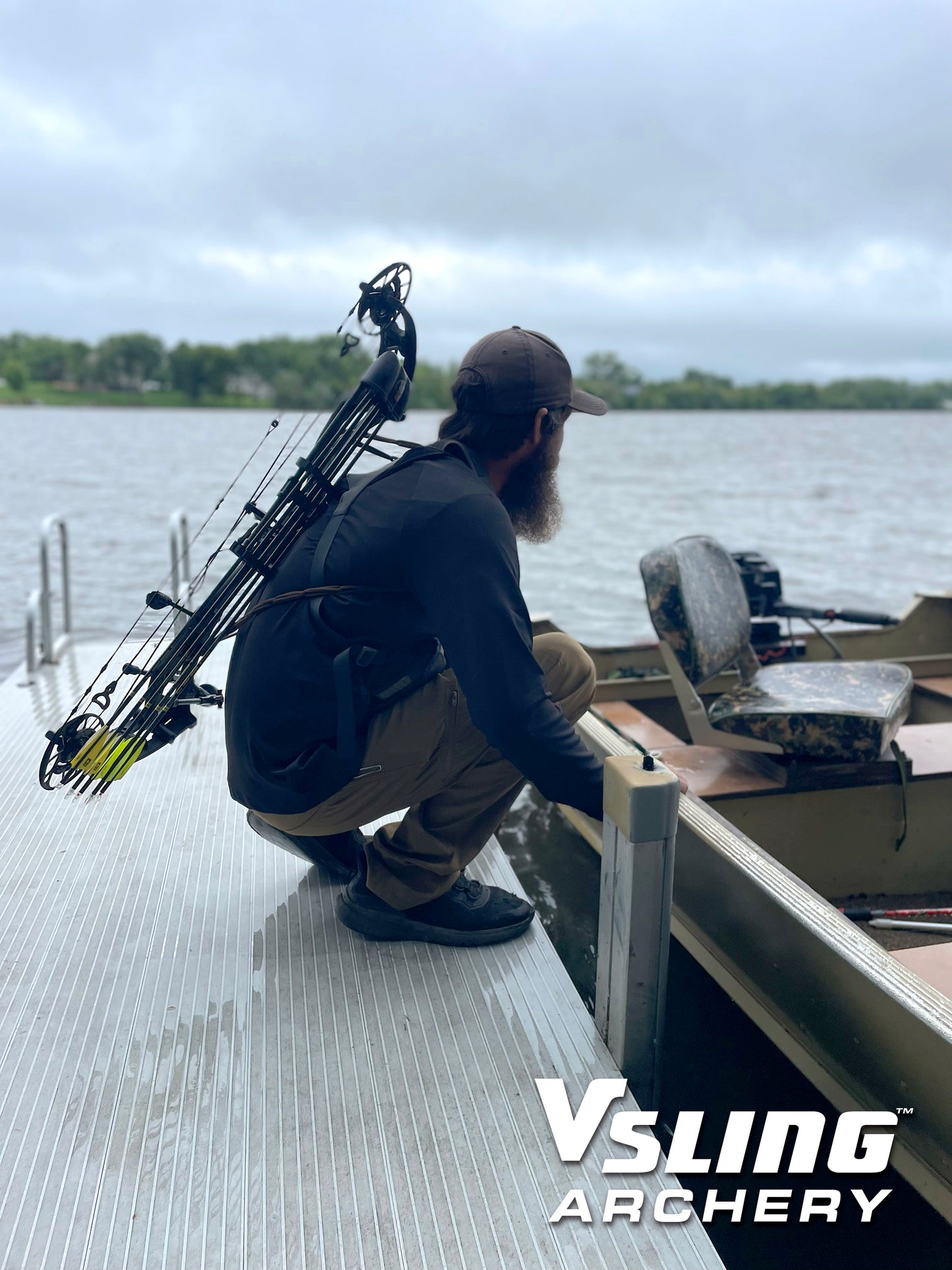 Man with a bow and arrow slung on his back on a dock by a lake, with 'Vsling Archery' branding