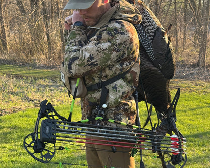 Hunter with a bow, vsling and a dead turkey in a grassy field