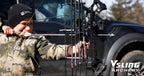 Person in camouflage holding a compound bow with a truck in the background, featuring VSLING ARCHERY branding.