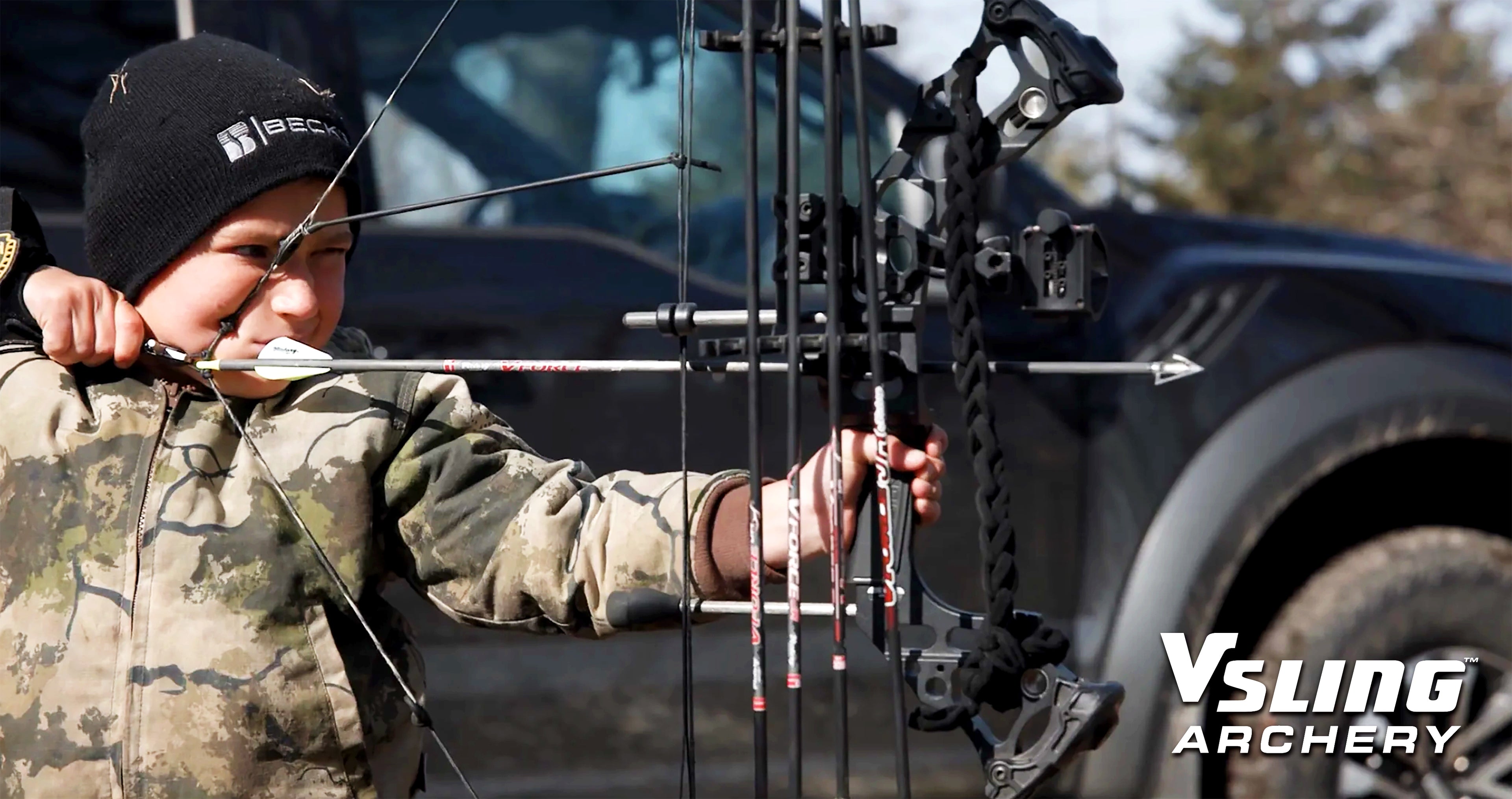 Person in camouflage holding a compound bow with a truck in the background, featuring VSLING ARCHERY branding.