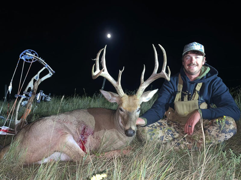 Man posing with a large deer at night with Vsling on his bow