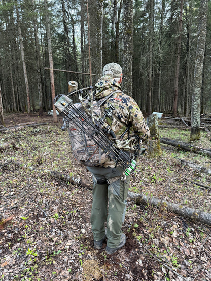 Person in camouflage gear and backpack with a bow secured by Vsling in Canada